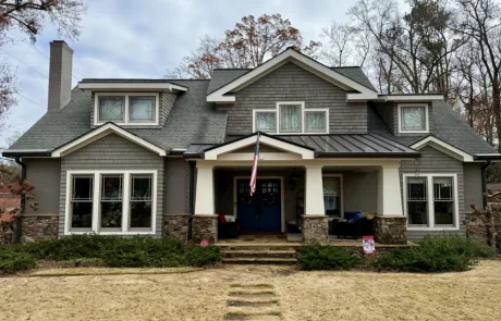 A large gray house with a stone porch and gabled roof proudly displays an American flag.