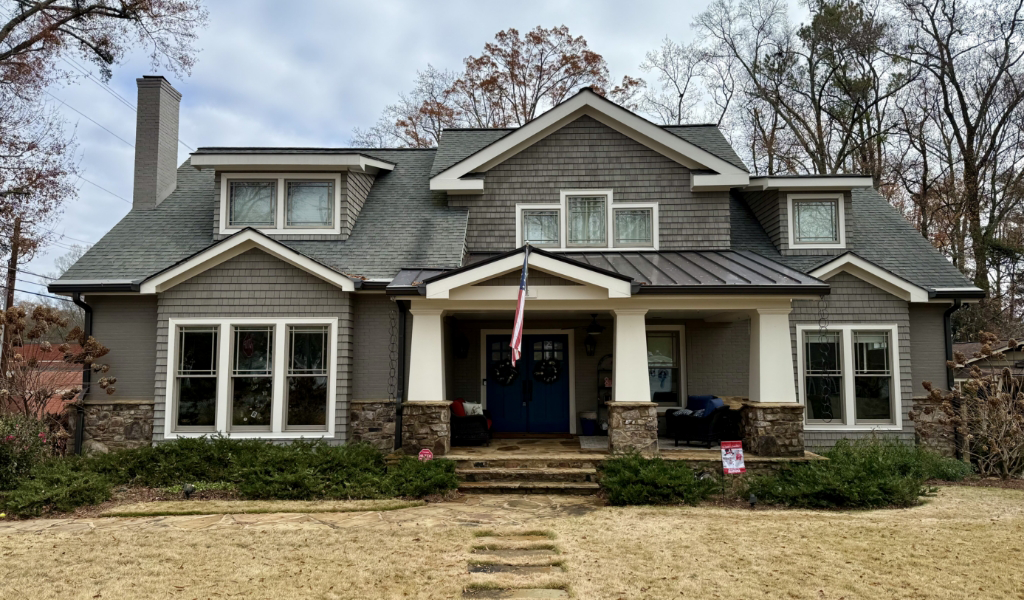 A large gray house with a stone porch and gabled roof proudly displays an American flag.