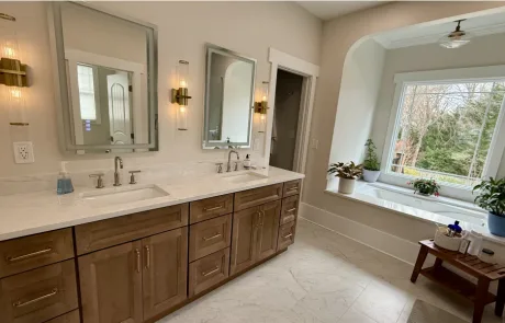 The bathroom boasts a double sink vanity, two mirrors, wall sconces, and a large window near the bathtub.