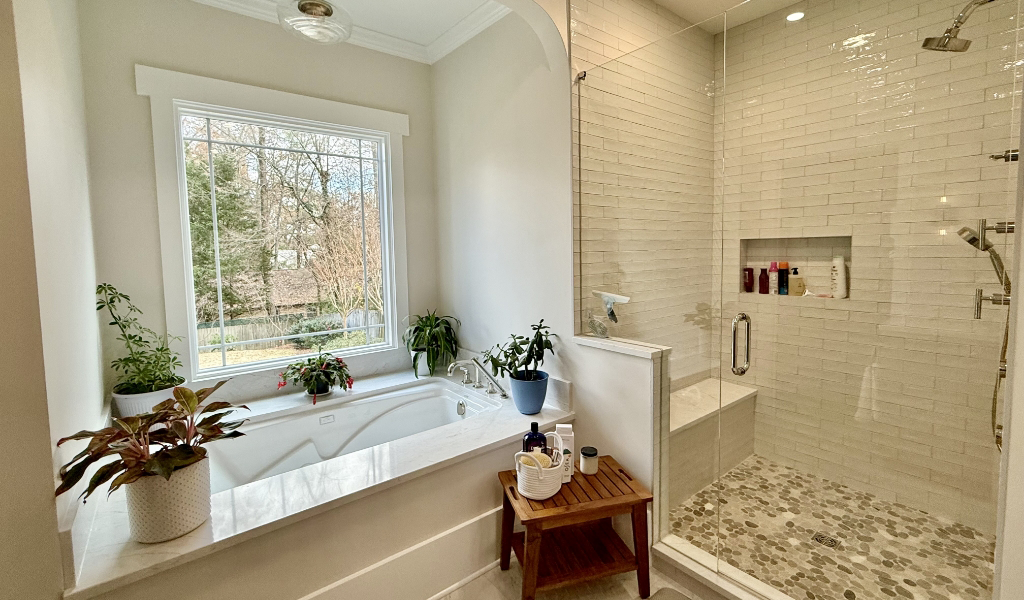 A bathroom features a large bathtub with plants nearby and a glass-enclosed shower with a tiled interior. A window provides natural light.