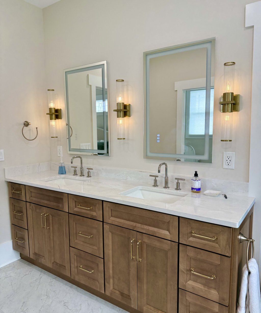 The bathroom features a double sink vanity with two rectangular mirrors and elegant brass light fixtures. The light-colored countertop adorned with soap dispensers complements the soothing beige wall.