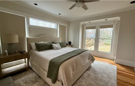 A bedroom painting project brings life to this serene space, featuring a large bed with green and white bedding, flanked by two nightstands.